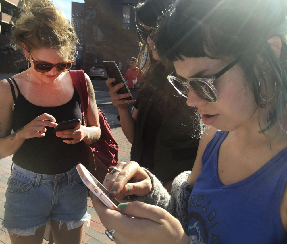 Monument Square in Portland was a hot spot of activity for the Pokemon Go "augmented reality" game Monday evening. From left, Shellbe Flynn, Jordan Regios and Elizabeth Hook play the game.