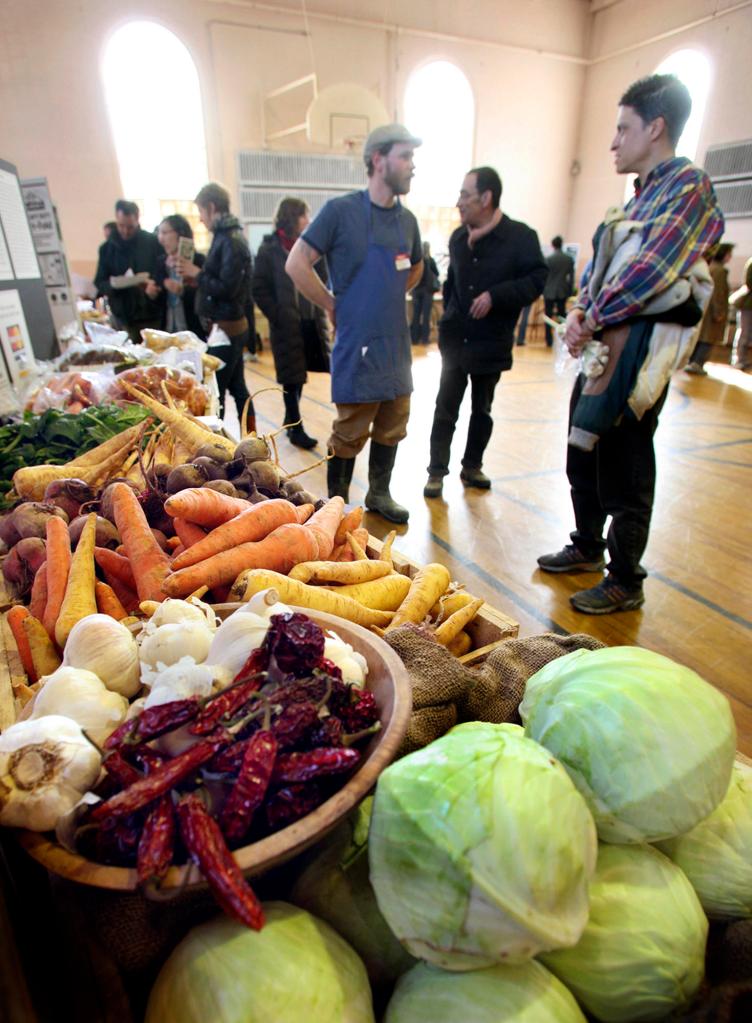 Chris Cavendish of Fishbowl Farm in Bowdoinham, left, and Randy Woods of Portland discuss Woods’ share with the farm at the Woodfords Congregational Church on Sunday.