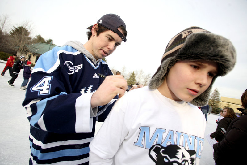 Ryan Hegarty, who went through the United States under-18 national team program before joining UMaine, signs an autograph on a shirt worn by Logan Fortin, 10, of Fairfield.