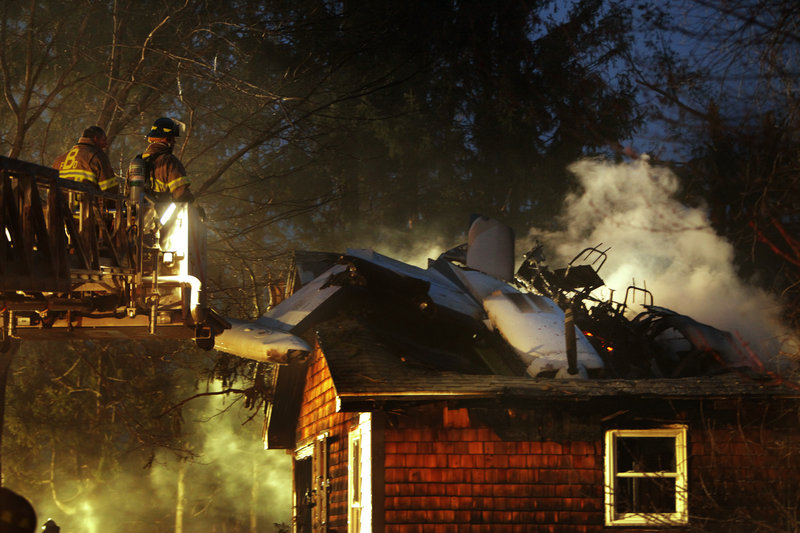 Biddeford firefighters maneuver a ladder closer to an airplane that crashed into a house on Granite Street Extension in Biddeford on Sunday night. Crews from Saco and Goodwins Mills also fought the fire.