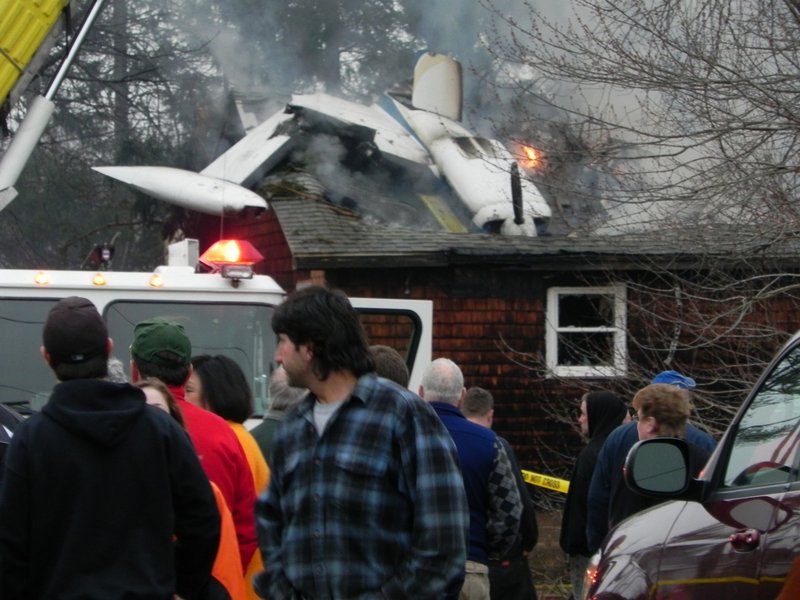 Neighbors and spectators gather at a home on Granite Street Extension in Biddeford after a small airplane crashed into it Sunday. The FAA confiirmed that one person died in the crash just after 6 p.m.