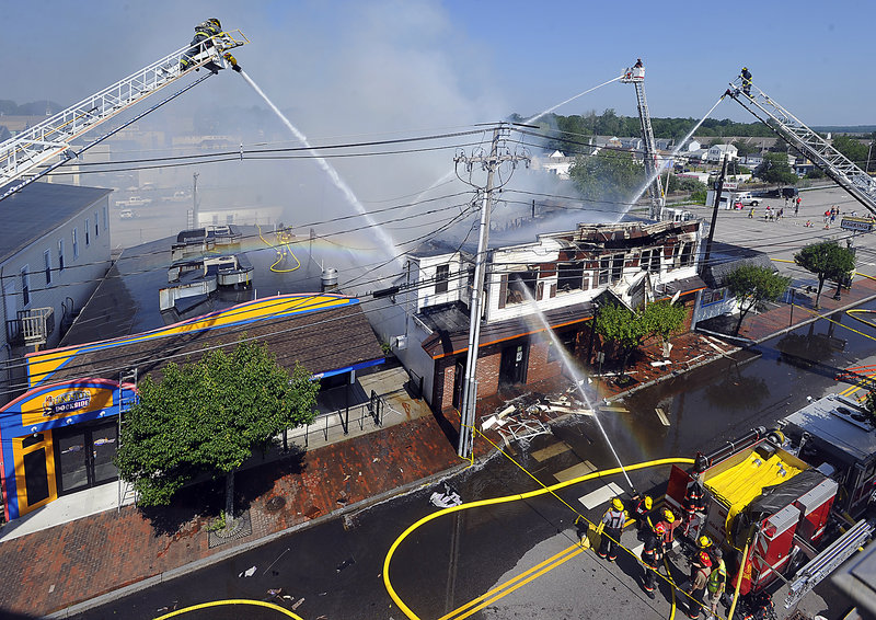 Firefighters on ladder trucks pour water onto the Galaxy nightclub Monday as it burns on East Grand Avenue in Old Orchard Beach. They were able to keep the fire from spreading to the businesses on each side of the Galaxy, which appeared to be undamaged.