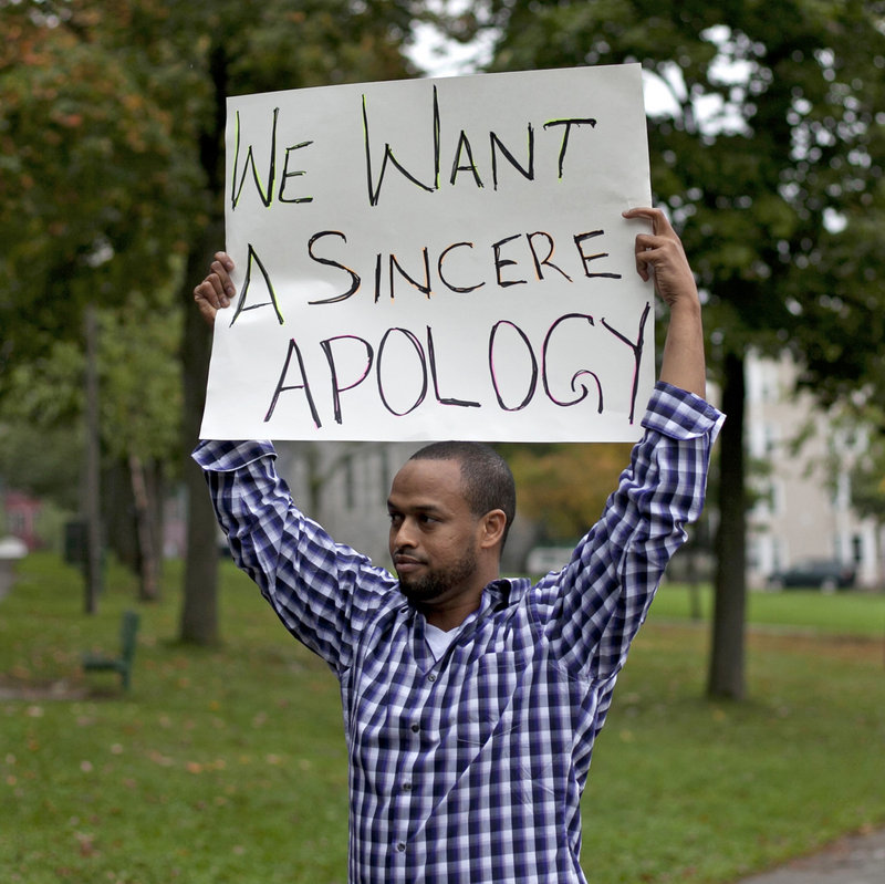 A man who joined Thursday’s rally holds a sign aimed at Lewiston Mayor Robert Macdonald, who answered his critics at a City Council meeting earlier in the week but refused to apologize. Those offended by his remarks about immigrant culture want him to apologize or step down.