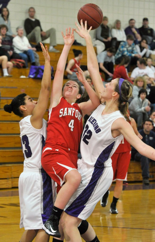 Morgan Fogg of Sanford gets fouled by Deering’s Marissa MacMillan, right, while Keneisha DiRamio also defends during their SMAA girls’ basketball game Thursday.