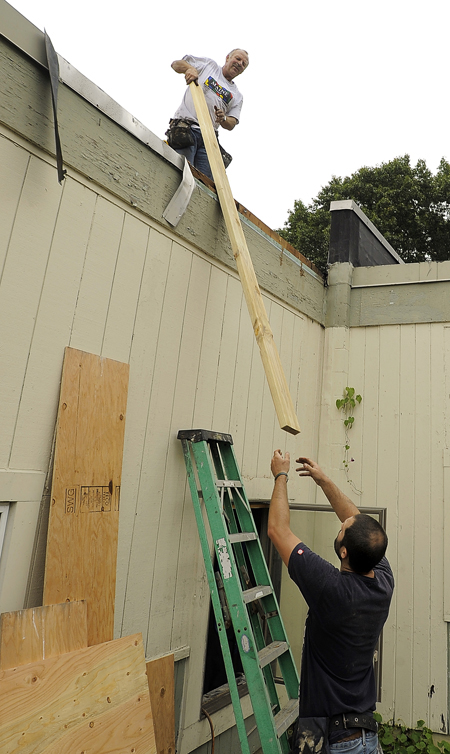 Gabe Souza/Staff Photographer: Bill Colby, left, top, of Colby Contractors in South Portland, receives a wood board from Aaron Gallagher, right, as the two work to seal the damaged roof of the Hall Elementary School before a storm blew in Tuesday, September 18, 2012, after a fire damaged the school earlier that week.