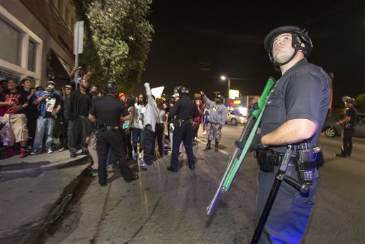 A police officer stands guard as demonstrators march on Crenshaw Boulevard near the I-10 freeway during a protest in Los Angeles on Sunday, July 14, 2013, the day after George Zimmerman was found not guilty in the shooting death of Trayvon Martin. Seventeen-year-old Martin was shot and killed in February 2012 by neighborhood watch volunteer George Zimmerman.