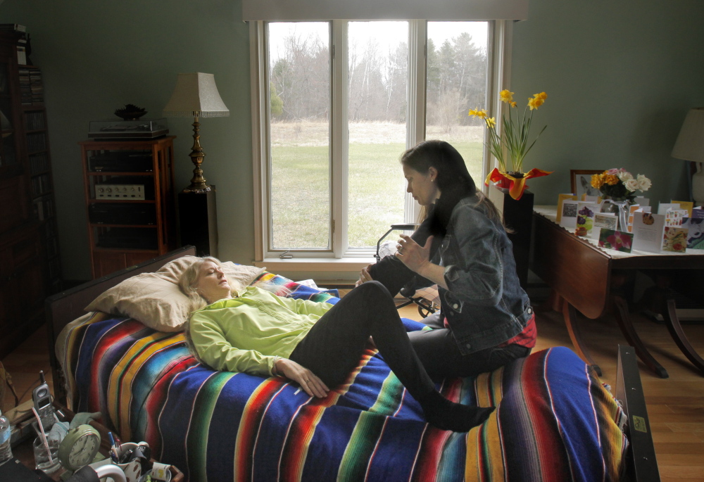 Eileen Whynot, 58, stretches with the help of her physical therapist, Sarah Dudley, at Whynot’s home in Gorham on Tuesday. Whynot broke her pelvis and left hip in a serious ski accident at Sunday River last month and is grateful for having purchased health insurance through the Affordable Care Act.