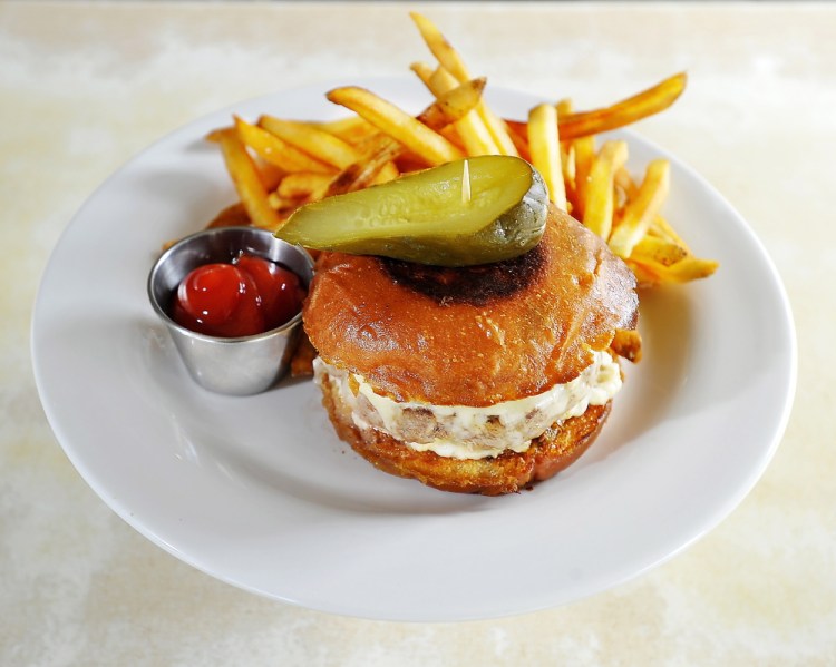 Grass-fed burger with griddled onion and sharp cheddar on a brioche bun, with crunchy fries, a pickle and ketchup.