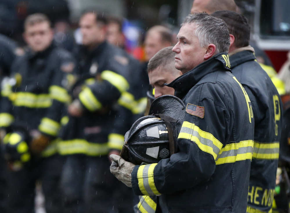 Firefighters take their helmets off as a body is removed from the scene of the fatal apartment building fire in Portland on Saturday.