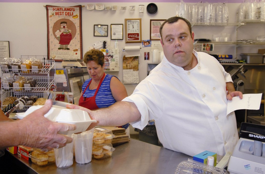 David Rosen hands a customer a to-go order while Goldie Gordius takes an order at the Full Belly Deli. The Brighton Avenue restaurant has closed, but its fans anticipate its reopening soon in the Old Port.