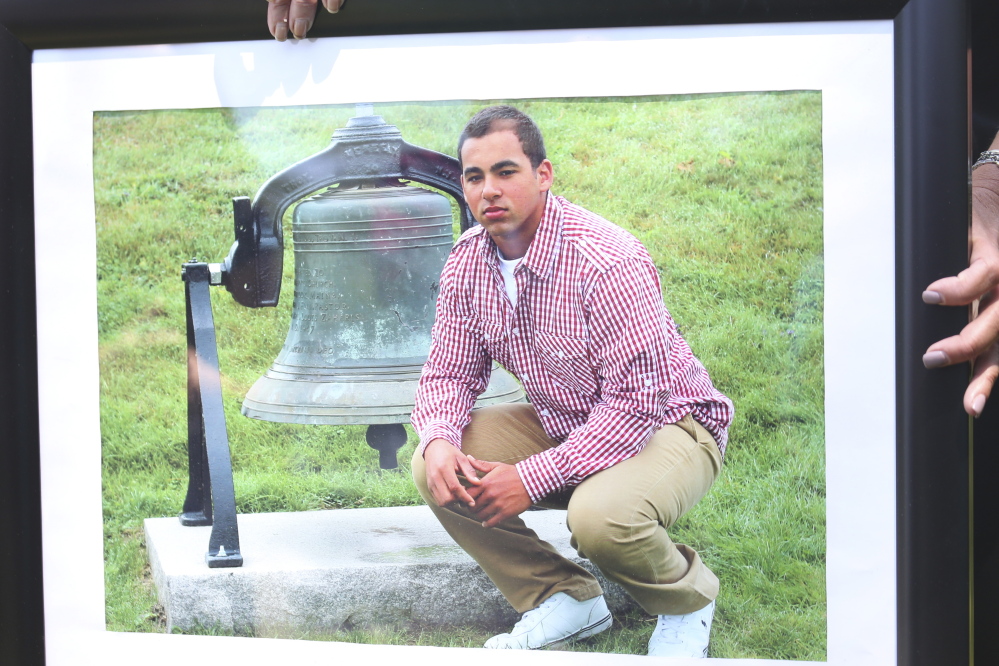 At her news conference Tuesday, Nancy Laxson holds a photo of her son, Treyjon Arsenault, in front of the victory bell at Westbrook High School.