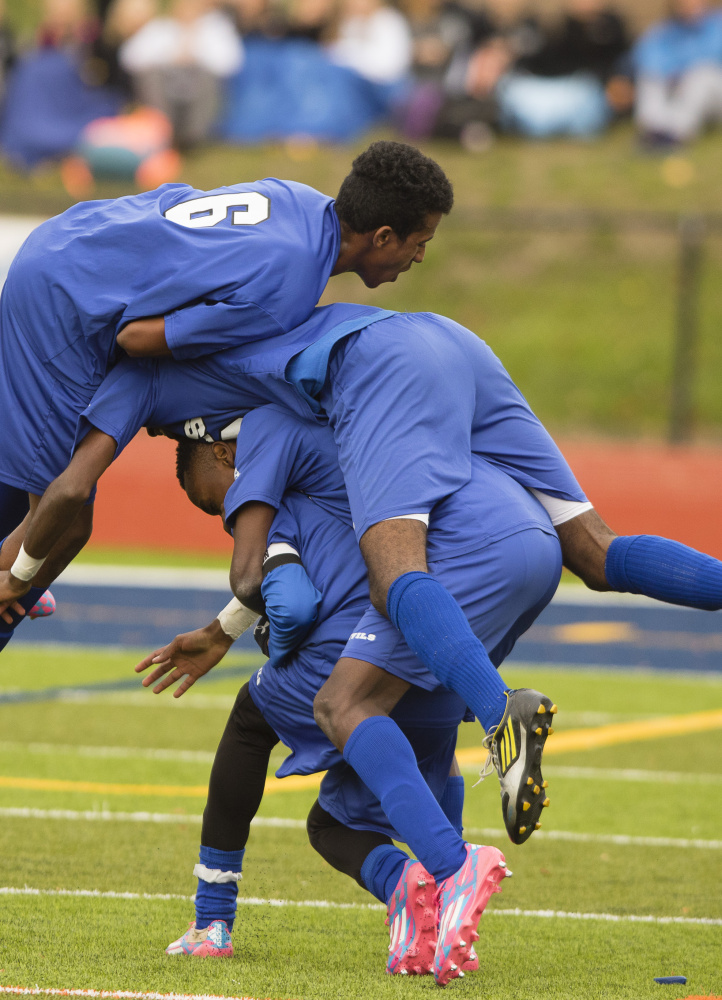 Lewiston High players pile on teammate Maulid Abdow after he scored the winning goal in the Class A state title game Nov. 7.