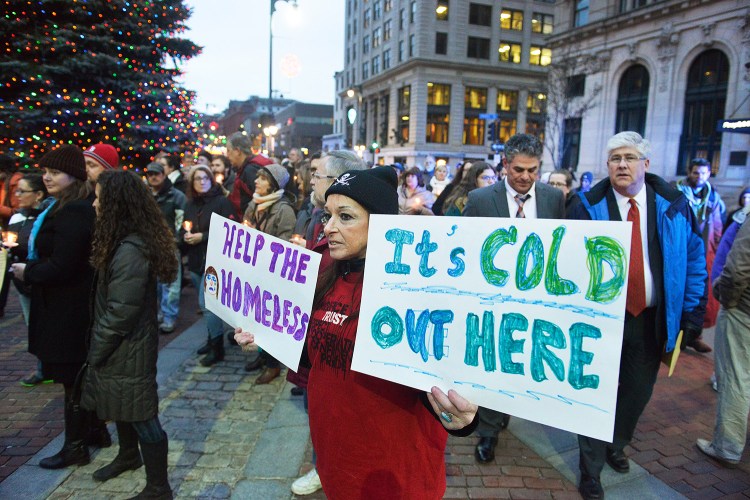 Portland's annual homeless vigil for homeless people who died in the past year marked a record number of deaths. Sally Reed-Hutchinson carries signs supporting the homeless and their needs during the vigil Monday in Monument Square. Behind her are Mayor Ethan Strimling, left, and City Councilor Nicholas Mavodones.