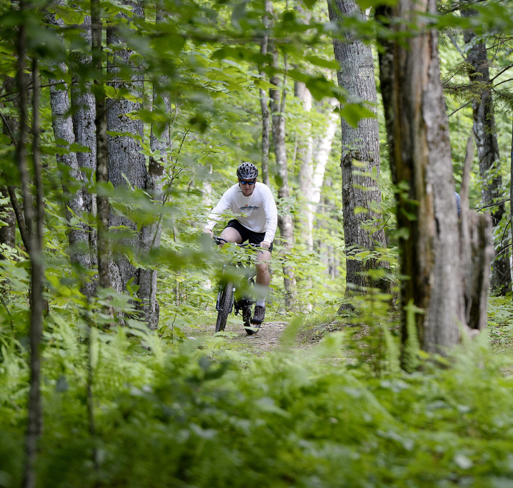 Ian Stewart, executive director of the Coastal Mountains Land Trust, bikes on what will soon be the Round the Mountain trail at Ragged Mountain in Camden.