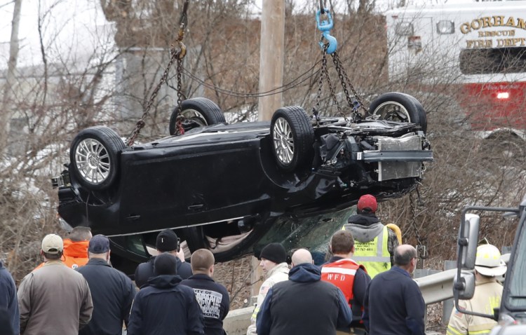 Police and firefighters watch Sunday as a tow truck lifts a car from the Stroudwater River along Spring Street in Westbrook.