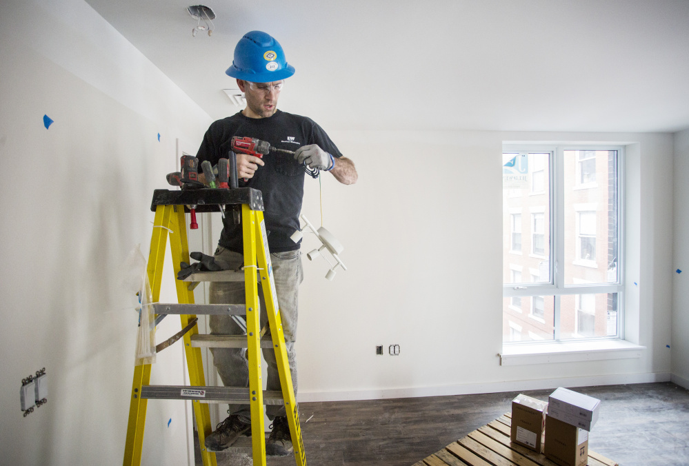 Seth Thompson, an electrician at B.H. Milliken, hangs lighting fixtures in an apartment at the Hiawatha building in Portland on Friday.