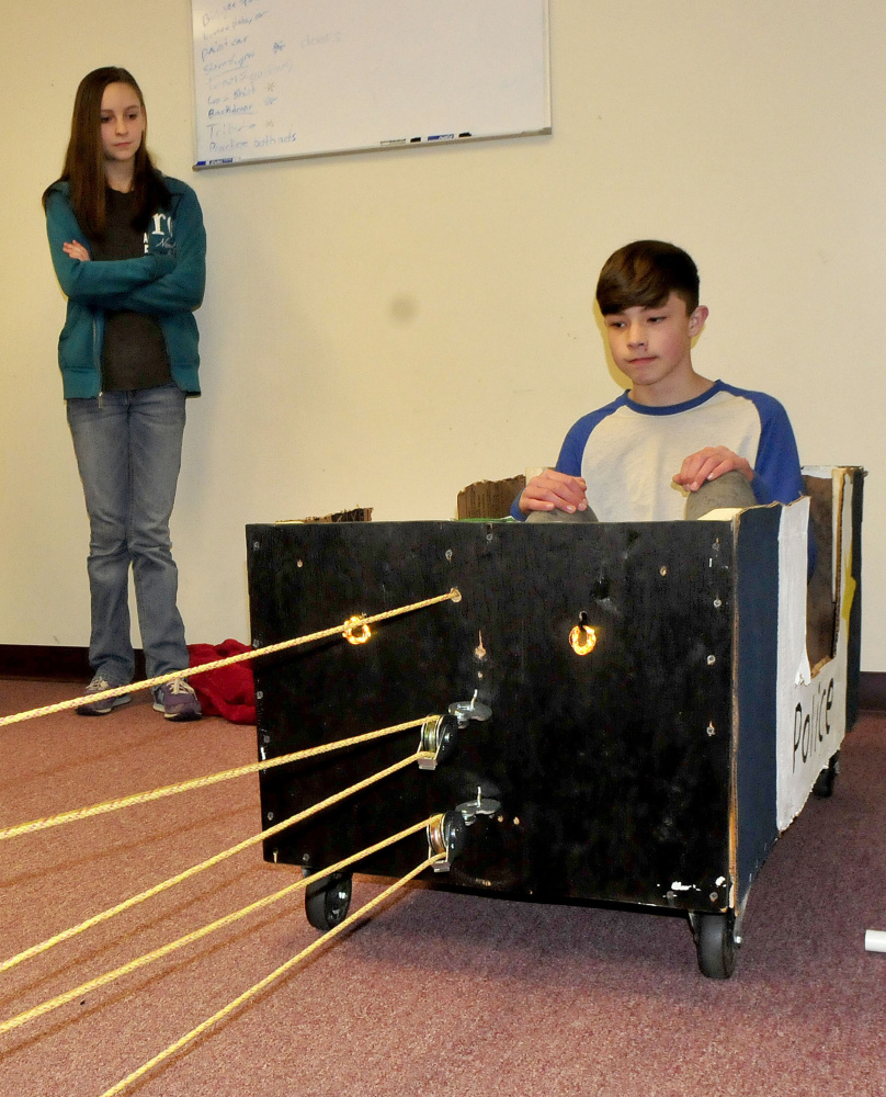 Ashton Umbrianna sits in a vehicle as another student  uses a device powered by a drill to pull it.