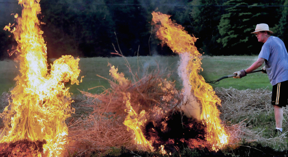 Peter Clifford throws a pitchfork full of burning brush to ignite another pile in August. A bill to allow municipalities to issue their own permits stalled in the Legislature.