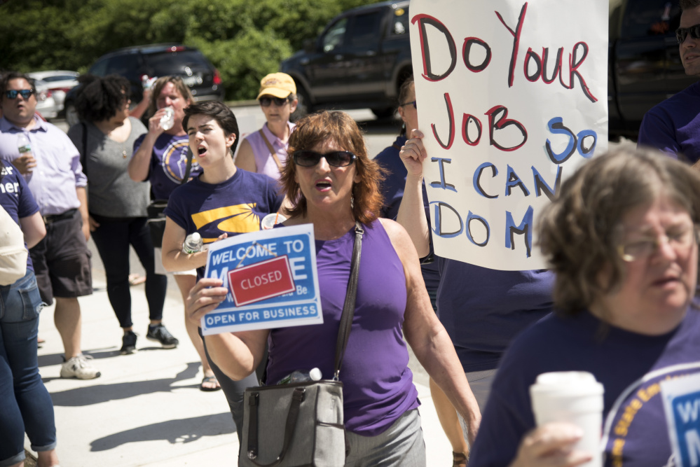 State employees and supporters march Monday in front of the Blaine House in Augusta on their way to the State House to protest day three of a state shutdown.