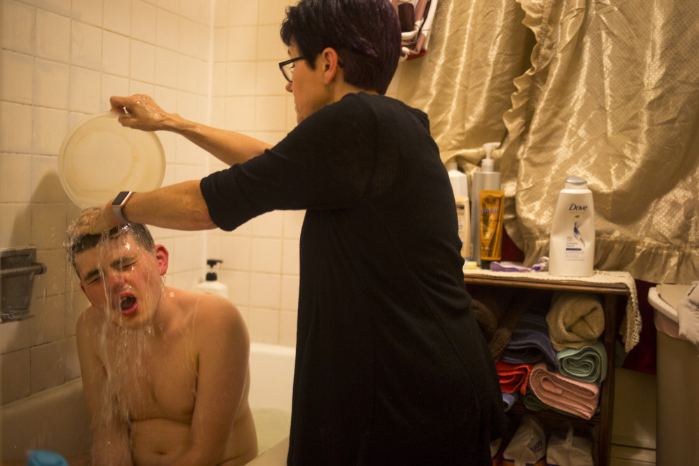 Donna Wall gives her son Christopher a bath Thursday. Because Wall lacks insurance coverage and is five years shy of Medicare eligibility, she can't afford doctor visits. Last year, she had soreness after falling on her tailbone, but she fears the day when she suffers an even more serious injury. Staff photo by Brianna Soukup