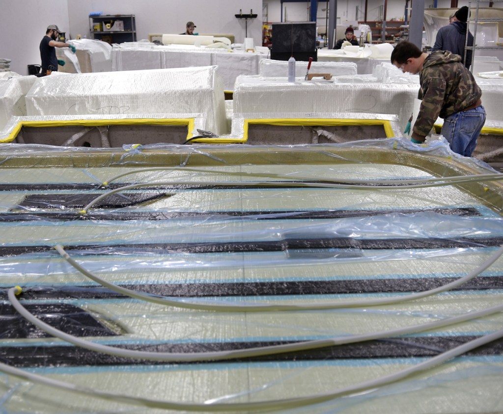 Employees of Southport Boats cut and hang fiberglass on molds Monday as a machine in the foreground infuses resin for a hard top at the firm's new location in Gardiner. Formerly part of Augusta's Kenway Corp., Southport has relocated to Gardiner under new ownership and will continue to produce its line of powerboats there.