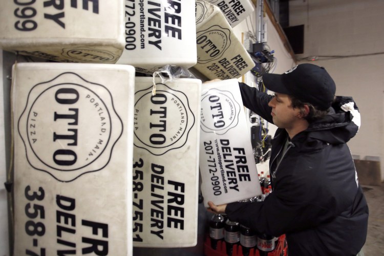 Nick Folan, a cook and fill-in delivery driver for Otto Pizza, pulls a magnetic sign from the wall of the franchise's location in South Portland. 