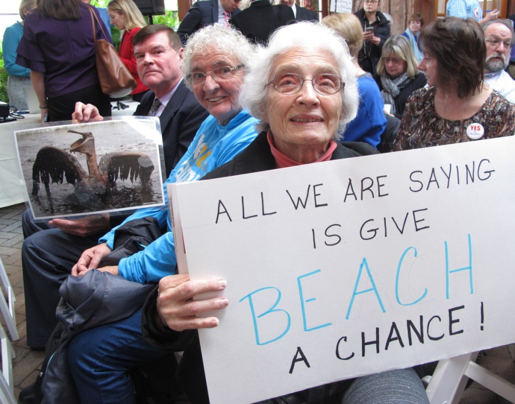 People hold signs protesting President Trump's plan to allow offshore oil and gas drilling along both of the nation's coasts during a hearing Wednesday in Hamilton, N.J. The public is not allowed to speak to attendees at the meetings and are asked to type comments on laptops provided by the Bureau of Ocean Energy Management.