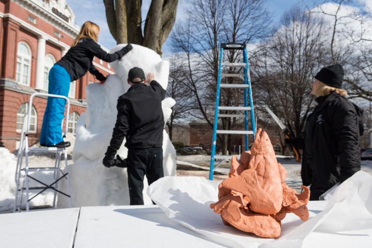 Starting from a clay model and a grid sketch, Cathy Thompson, right, watches as her children, Amanda Bolduc, left, and Chris Thompson carve a fish from a block of packed snow.