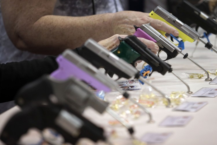 Attendees look over a pistol display at the National Rifle Association's annual convention in 2014. Over a dozen companies, including Metlife, Hertz, Avis, Enterprise, Best Western, Wyndham, United Airlines and Delta, have ended NRA partnerships since the Feb. 14 school massacre in Parkland, Fla.