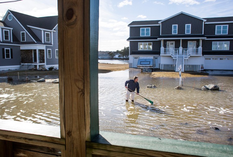 Dave Twomey, assistant building inspector in Saco and resident of Camp Ellis, uses a rake to try and find a drain on North Avenue on March 5. Several streets have been washed out and North Ave. has remained flooded since Friday's storm.