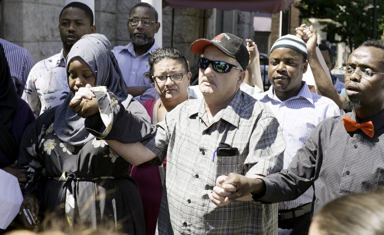 Jim Thompson holds hands with Fowsia Musse, left, and Abdi Abdalla during a gathering in Lewiston Sunday aimed at defusing ethnic tensions. Thompson is the uncle of Donald Giusti, who died from injuries he received in a brawl Tuesday.