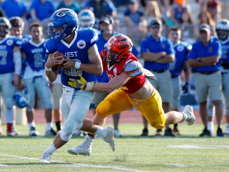 West quarterback Jack Bryant of Falmouth is brought down by East's Ryan Fredette of Winslow. The East defense played a key role in the team's surprising 40-14 win Saturday in Saco.