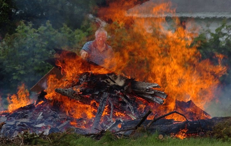 Steve Davis throws wood from an old building onto a burning pile in June 2017 behind his home on Lower Ridge Road in Fairfied. Davis said the wet conditions are ideal for burning. With the passage of L.D. 1809, burn permits can be obtained free from a private source online, Warden's Report.