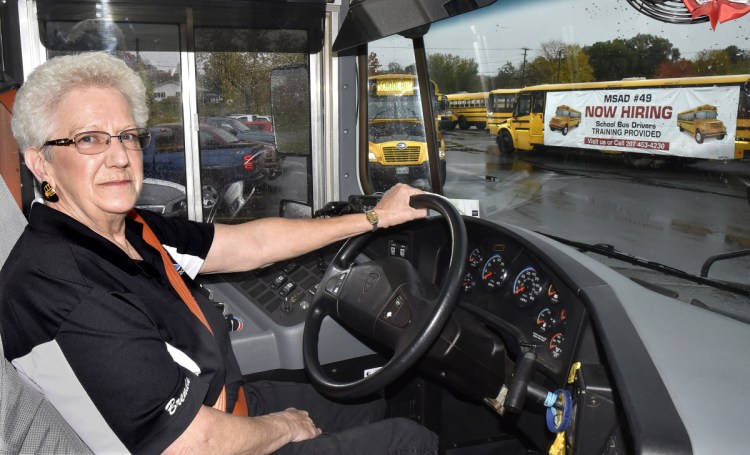 SAD 49 school bus driver Brenda Emery settles into her bus before picking up students at Lawrence Junior High School in Fairfield on Thursday. Outside is a bus with a sign that states the school system is hiring drivers. Emery has been a bus driver for 33 years and said she loves her job.