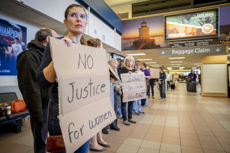 Delina Malo-Juvera holds a sign Sunday at the Portland International Jetport.