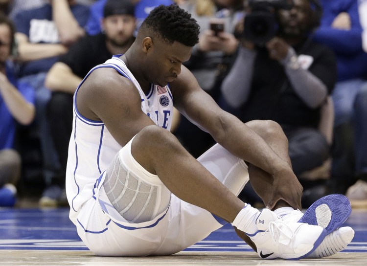 Duke's Zion Williamson, 18, sits on the court with his Nike sneakers, one ripped apart, after an injury during Wednesday's game against North Carolina.