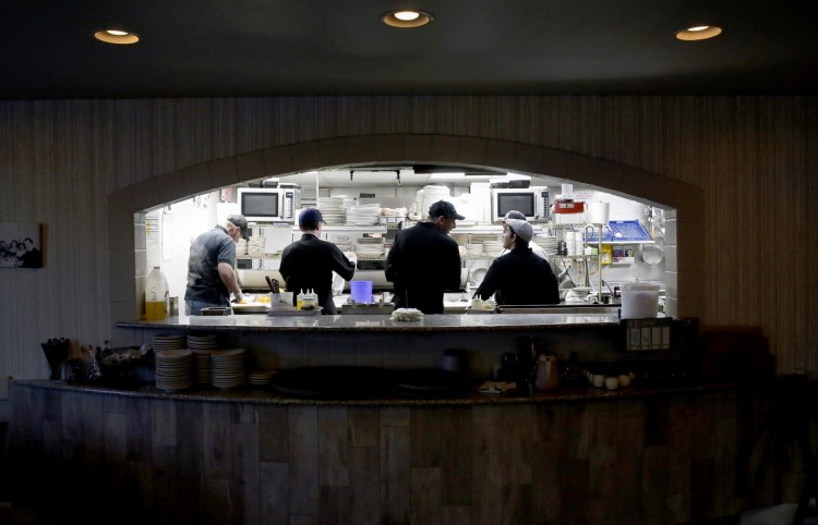 Kitchen workers at Bruno's Restaurant & Tavern glimpsed through a window that opens into the dining room.