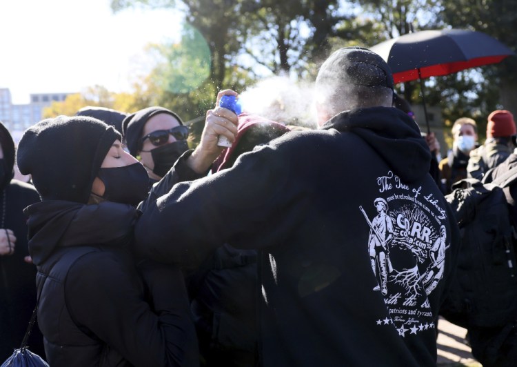 A counter protester, center left, releases a chemical irritant on a protester who came to attend what Super Happy Fun America and the Refounding Fathers Coalition called, "Rise Against Tyranny Rally," Sunday, as a scuffle brakes out between the two factions on the Boston Common. The counter protesters and demonstrators, opposing mask and vaccine mandates, clashed Sunday, leading to two arrests.